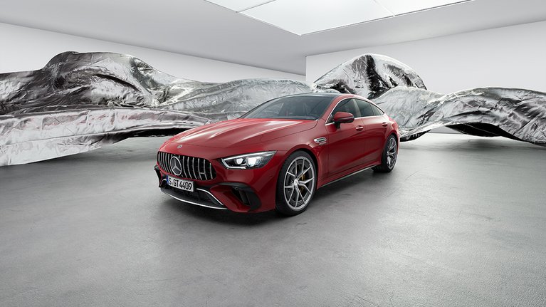 Mercedes-Benz AMG GT in Rot, Sicht leicht schräg von vorne, im Hintergrund ist ein abstraktes silbernes Kunstmodell